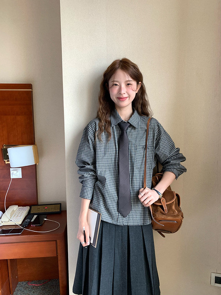 Woman in a checkered shirt and tie holding a brown bag in a room with a desk and lamp.