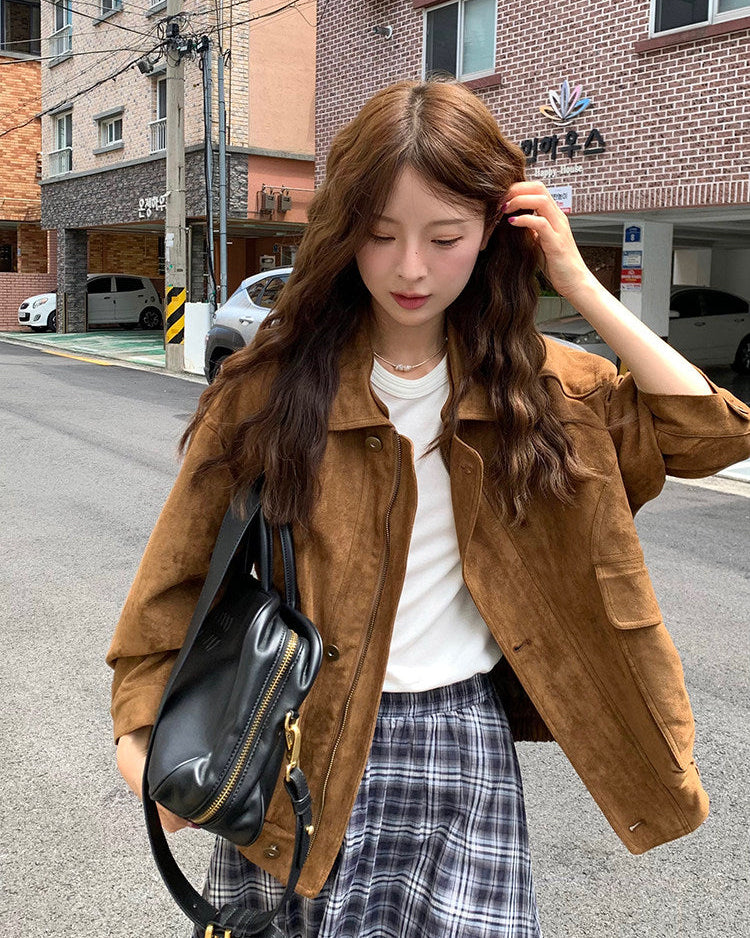 Woman in a brown jacket and plaid skirt standing on a street with buildings in the background